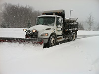 Entire scene covered in thick snow with large truck with a front snow plow making a large passageway.